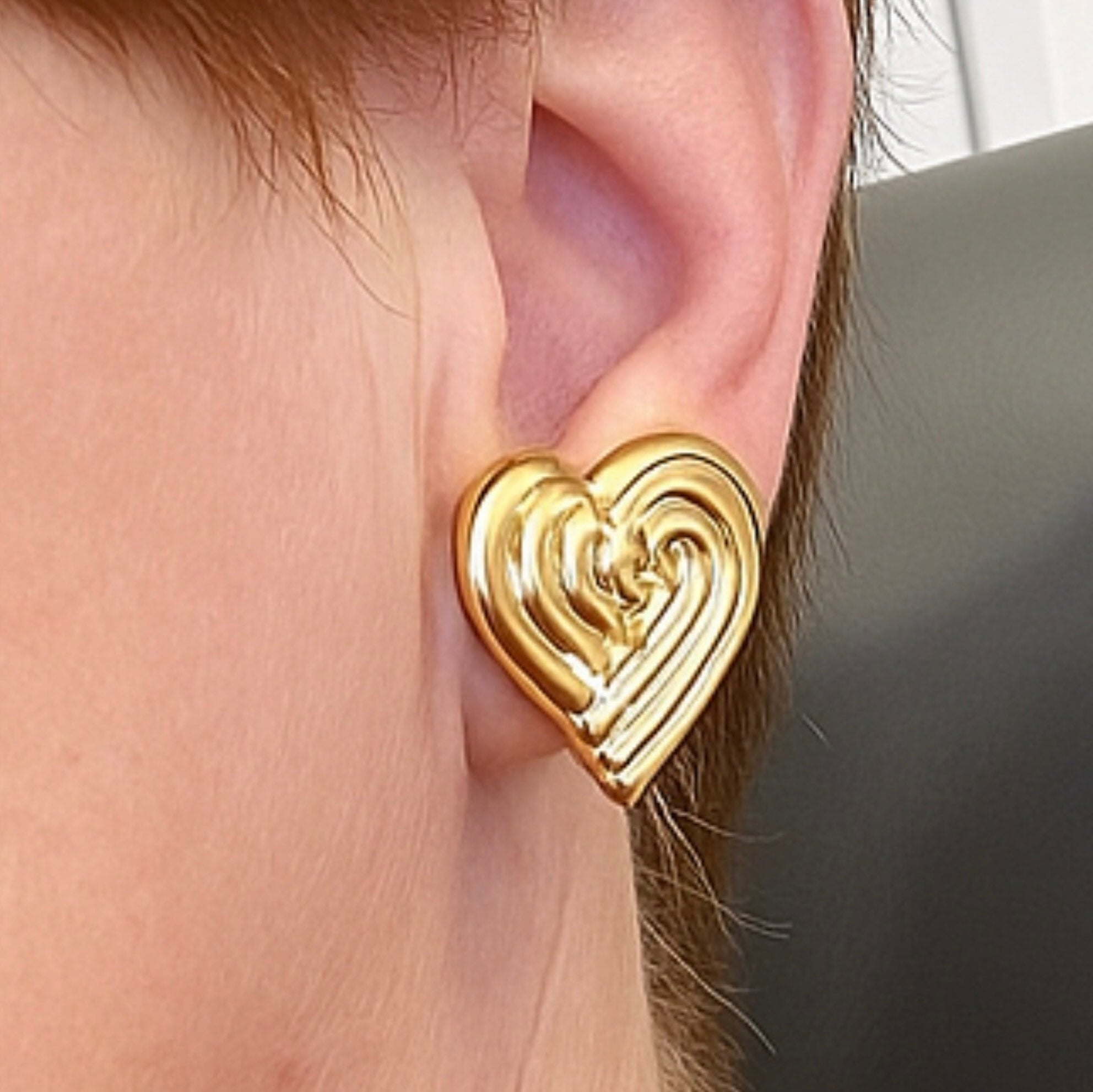 “Arete de botón en forma de corazón entrelazado de oro 14k con cierre omega, mostrado en la oreja”
