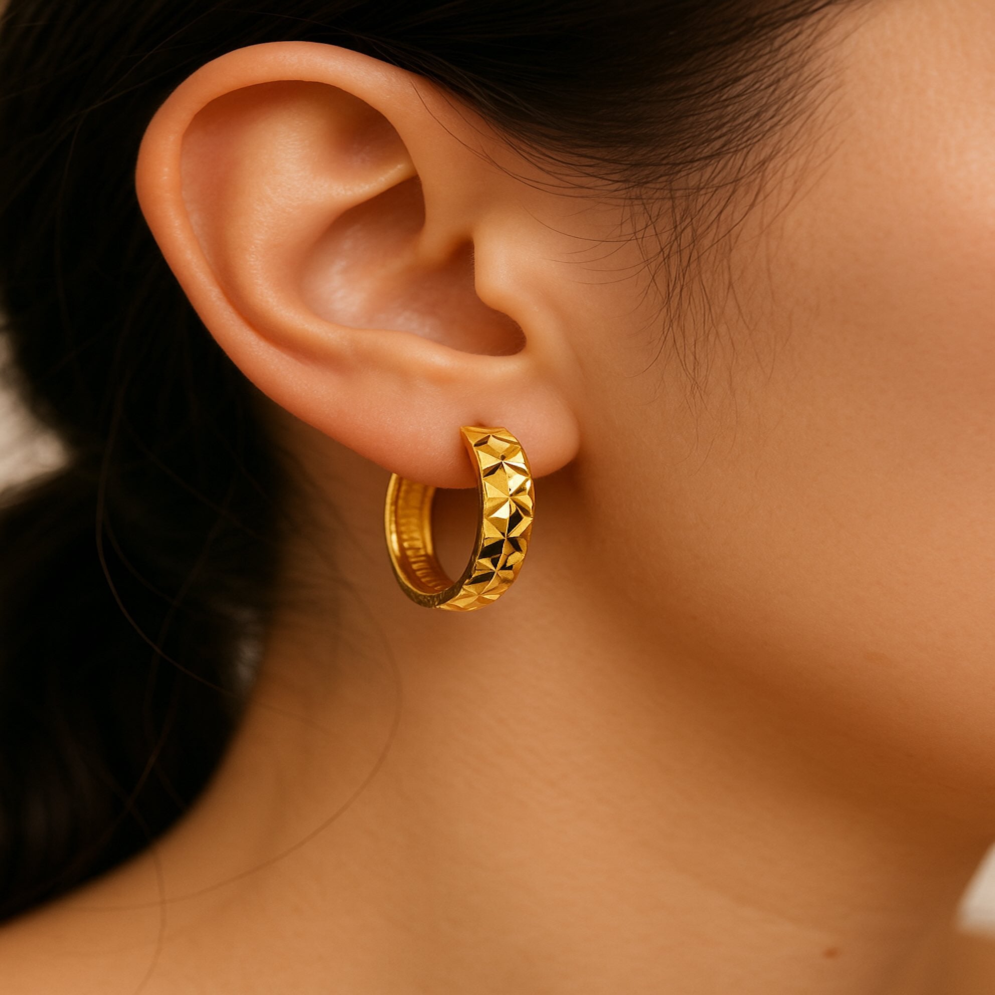 Arete huggie corto en oro 14K con diseño de corte diamante amarillo, en oreja de modelo para mostrar proporción real