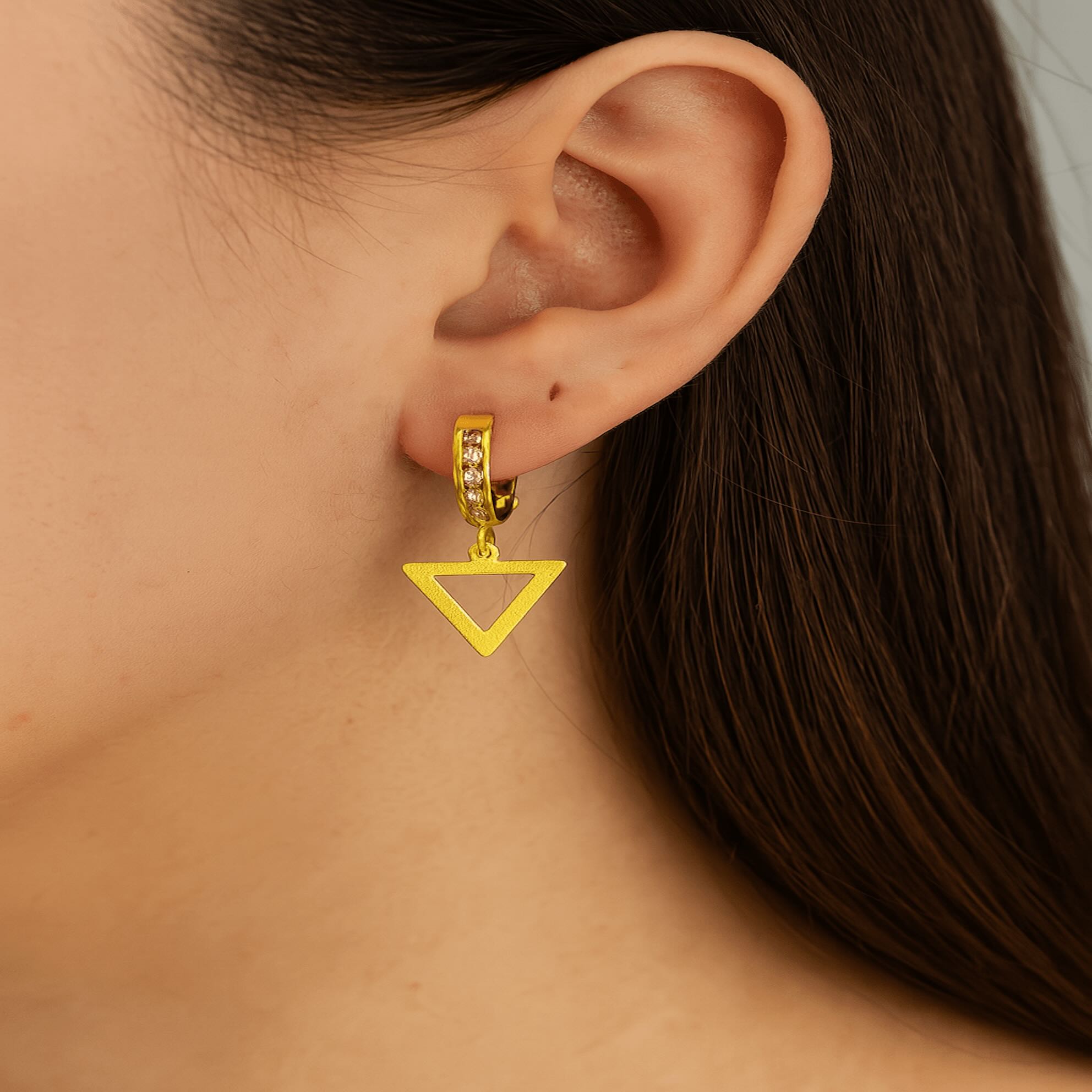 Arete mediano huggie en oro 14K con dije de triángulo y circonias brillantes, mostrado en oreja para visualizar su tamaño y caída
