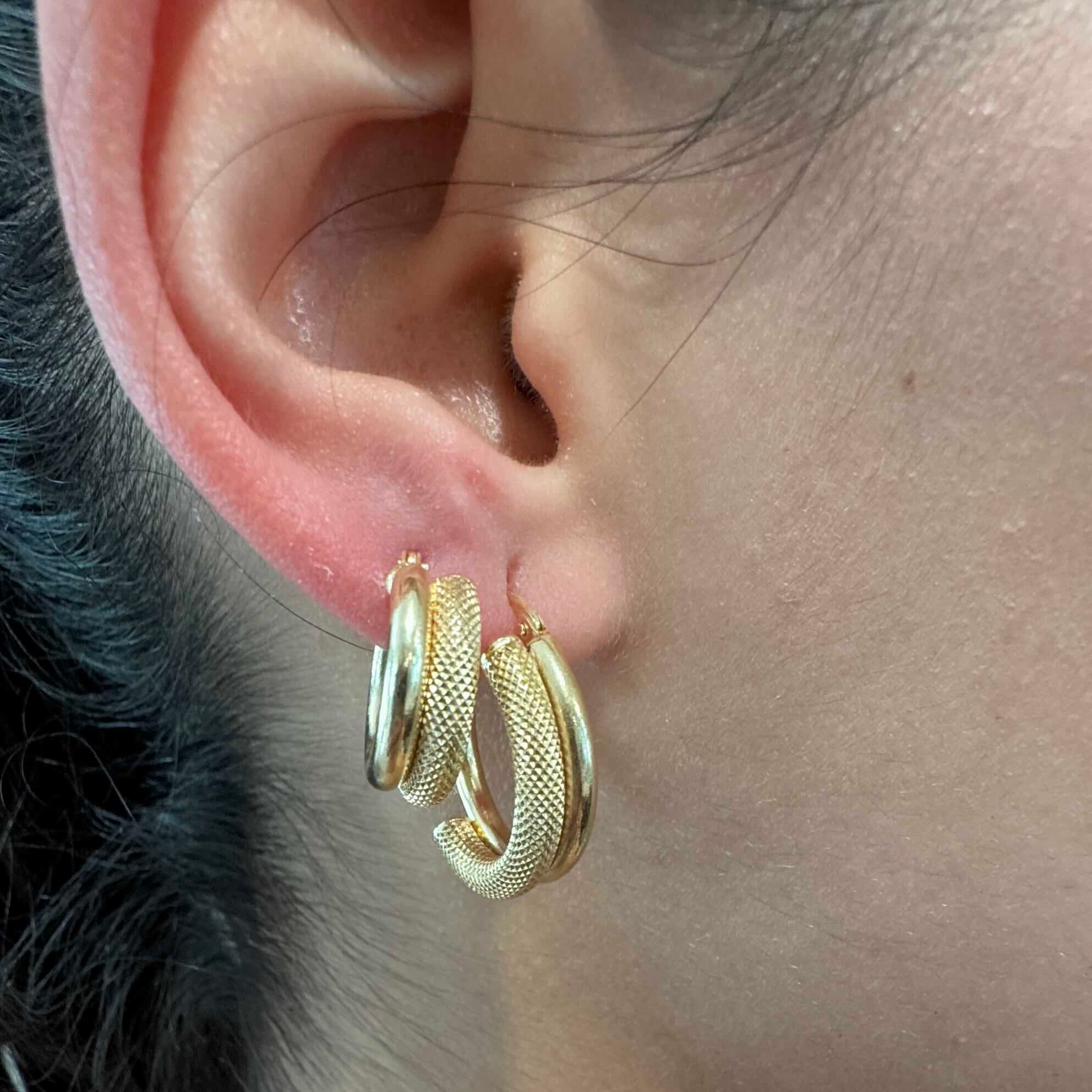 Aretes argolla medio aro satinado en oro 14K puestos en la oreja, modelo de doble tubo liso y satinado, disponibles en 15 mm y 20 mm.