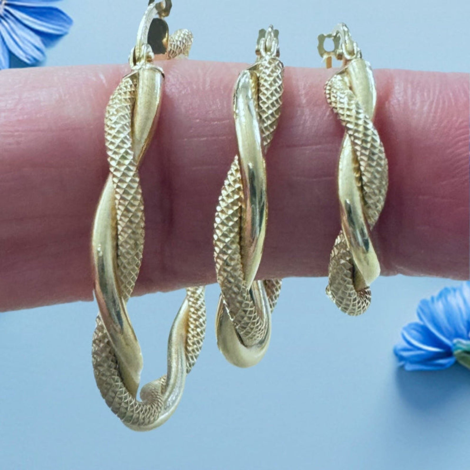 Detalle de aretes de oro 14K con diseño torcido dúo, acabado satinado y liso brillante, exhibidos sobre el dedo – Joyería TuOro