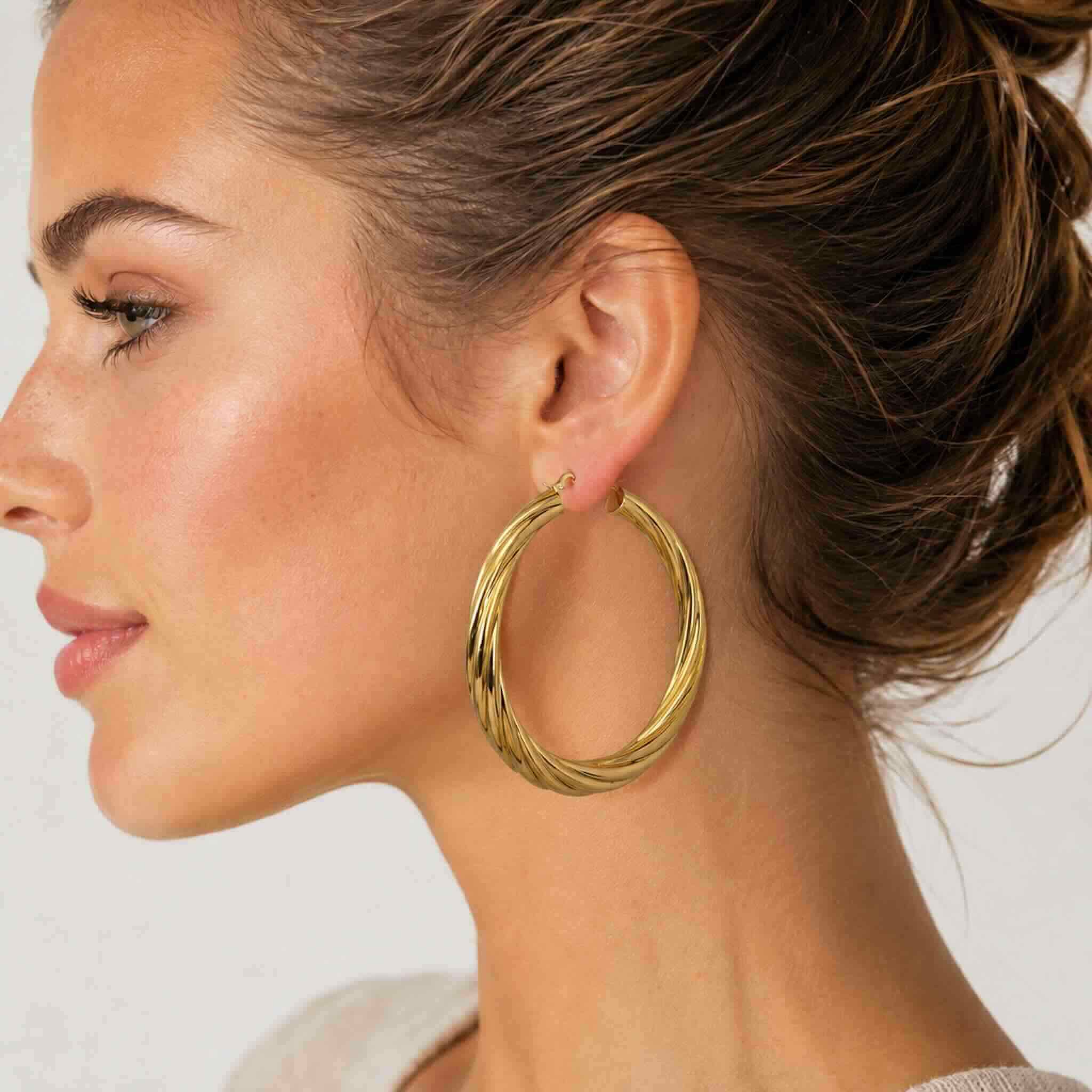 Mujer joven de piel clara con argollas torcidas lisas en oro 10K de 4.8 mm y 44 mm de diámetro.