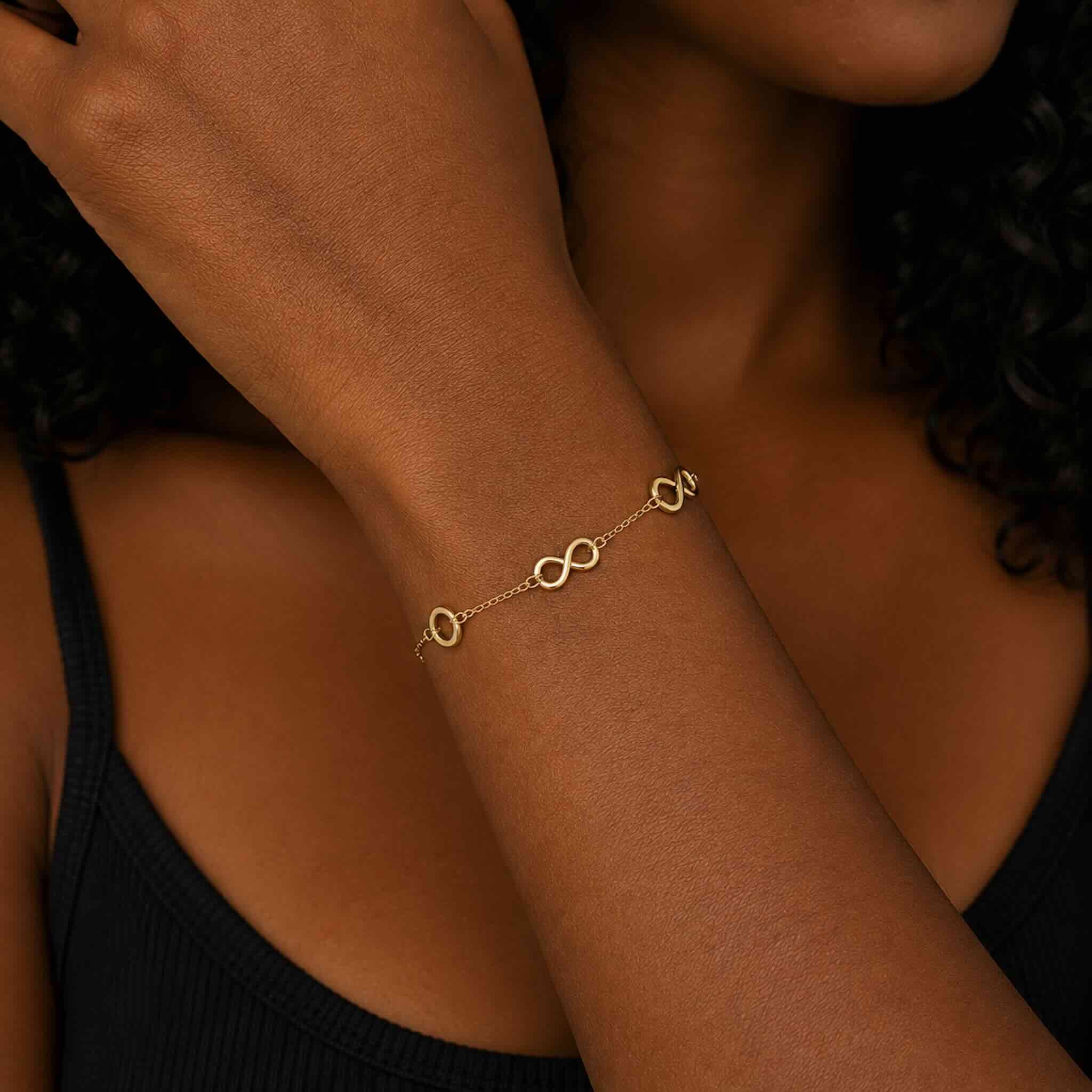 Vista completa de la pulsera delicada de oro 10K con símbolos de infinito usada por modelo trigueña en TuOro®.