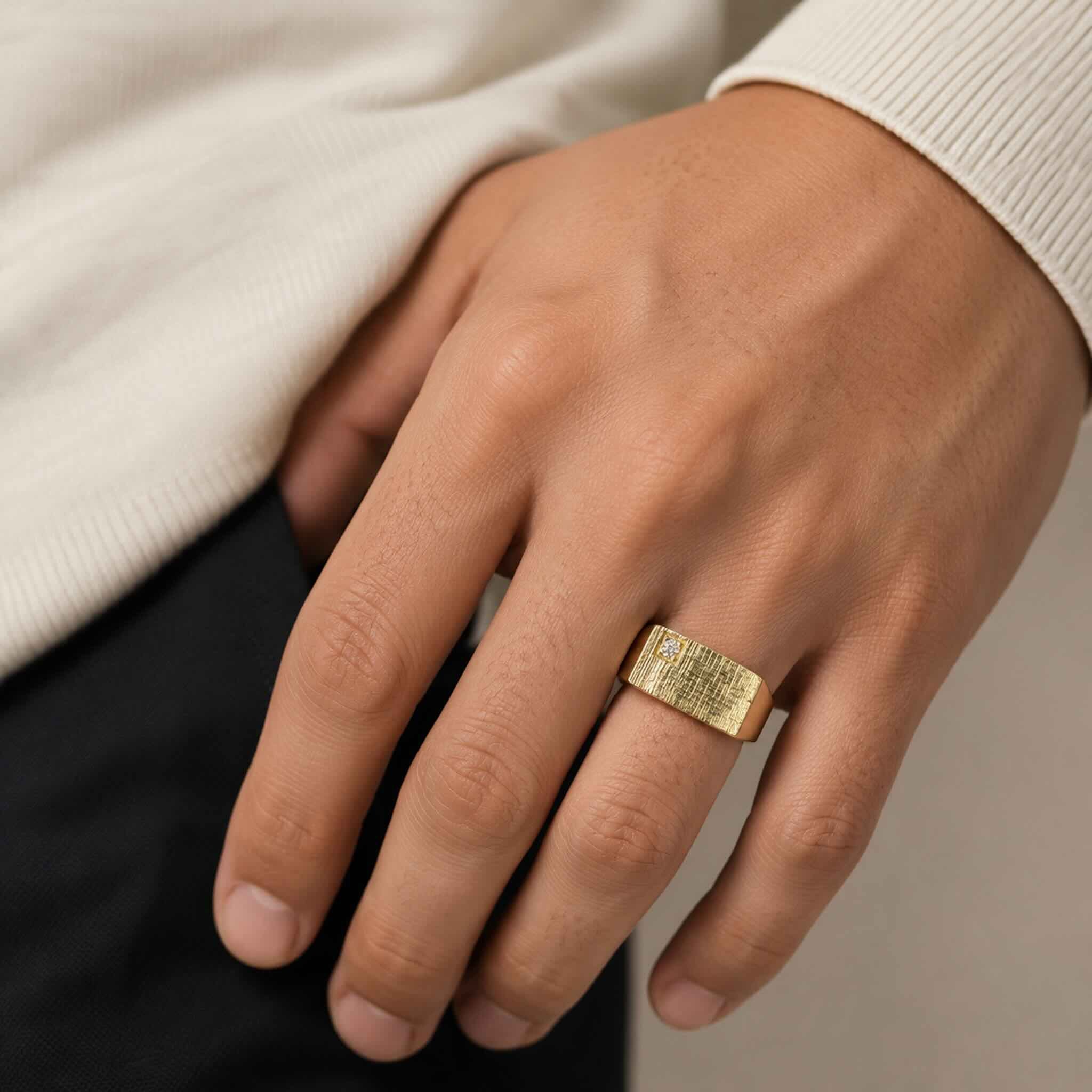 Primer plano de Anillo de Sello para Meñique en Oro 14K de TuOro con textura y circonia en la mano de un hombre joven, foto de catálogo.