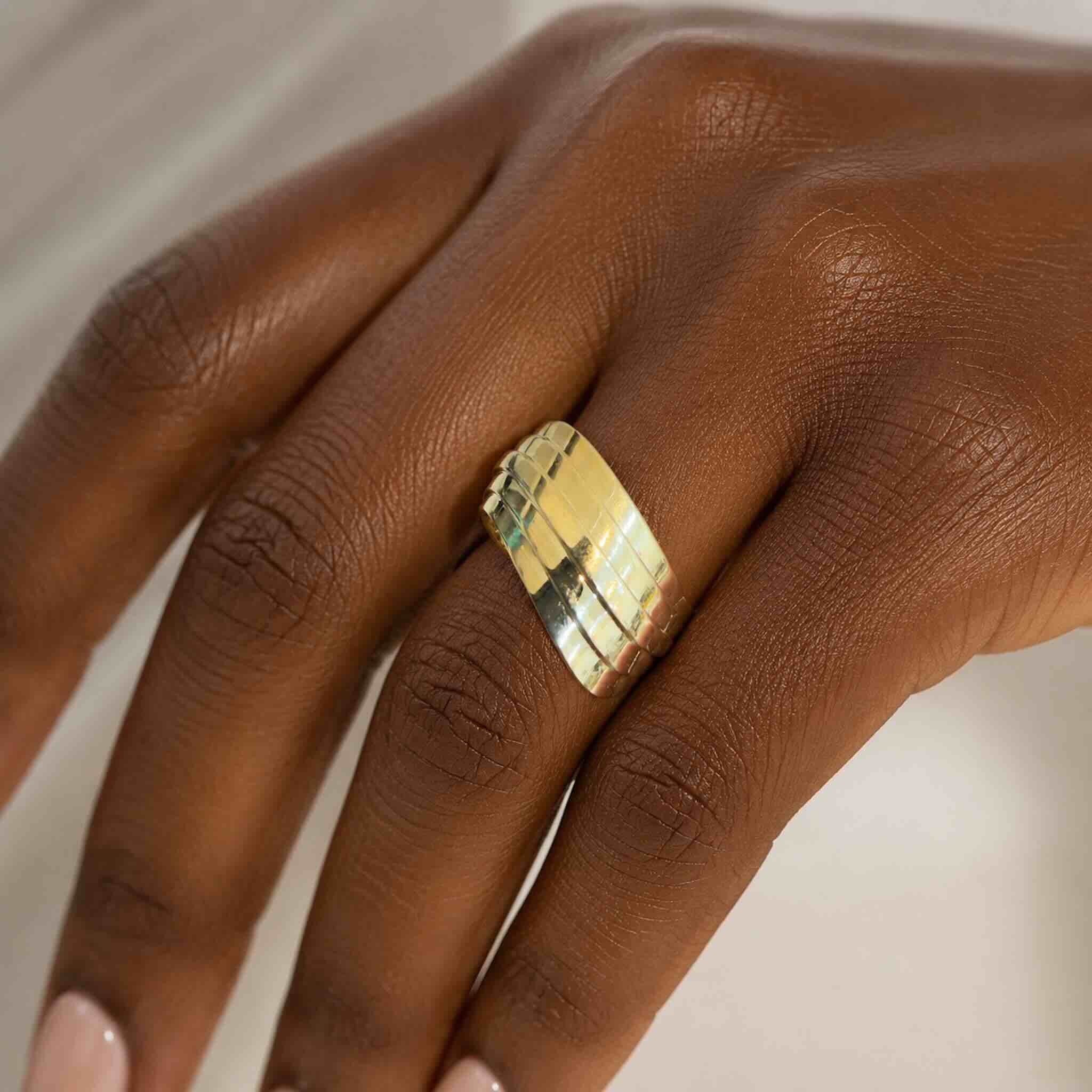 Anillo llamativo en Oro 10K con galería y diseño voluminoso de líneas pulidas, mostrado en la mano de una mujer elegante, TuOro®.