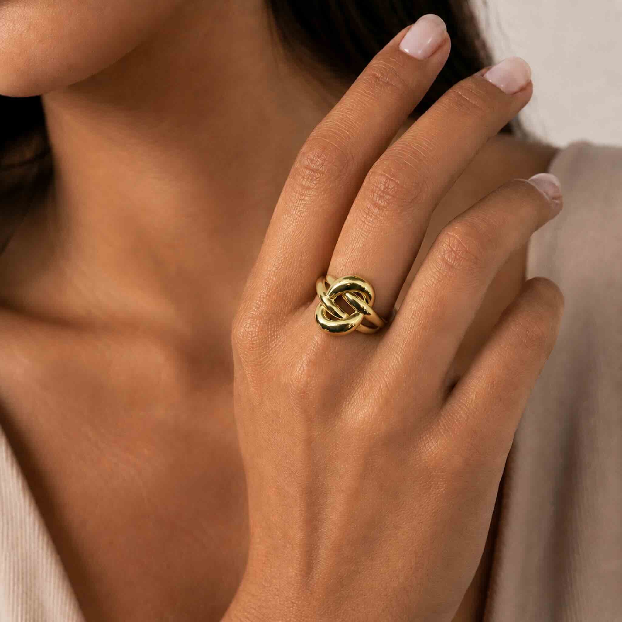 Anillo llamativo en Oro 10K con diseño tipo nudo modelado en la mano de una mujer trigueña joven, imagen de catálogo de TuOro®.