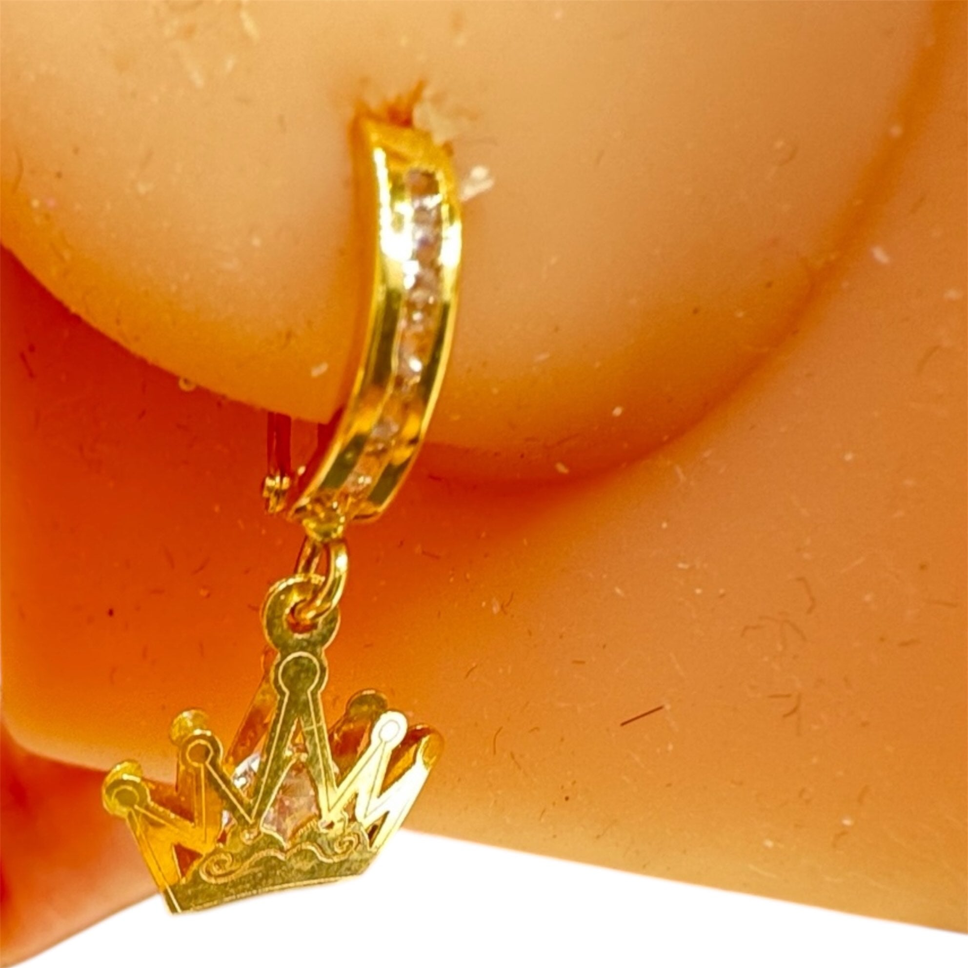 Arete mediano huggie en oro 14K con dije de corona y circonias brillantes, mostrado en maniquí para visualizar el tamaño real

