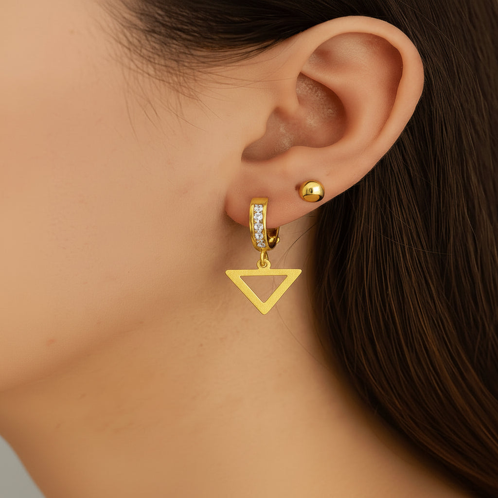 Arete mediano huggie en oro 14K con dije de triángulo y circonias brillantes, mostrado en oreja para visualizar su tamaño y caída


