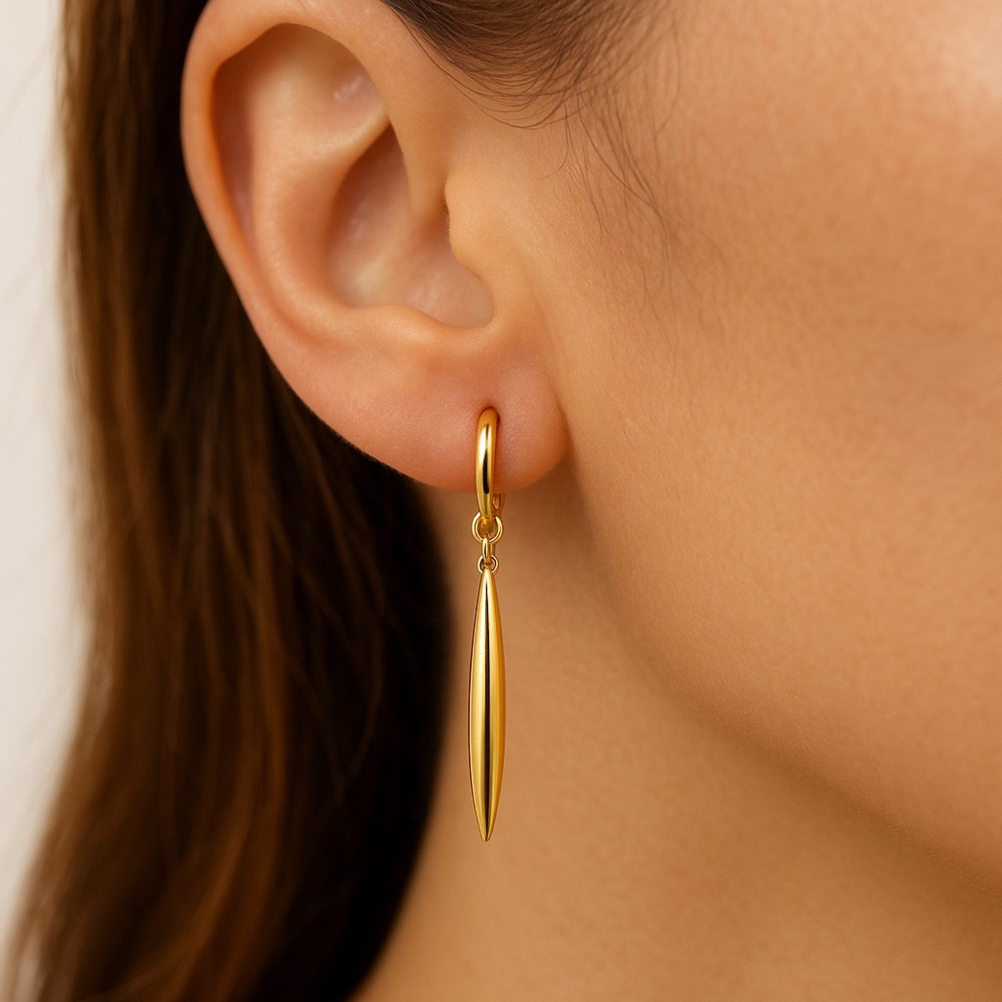 Arete largo huggie en oro 14K con diseño tipo espiga estilizada, mostrado en oreja para visualizar su caída elegante

