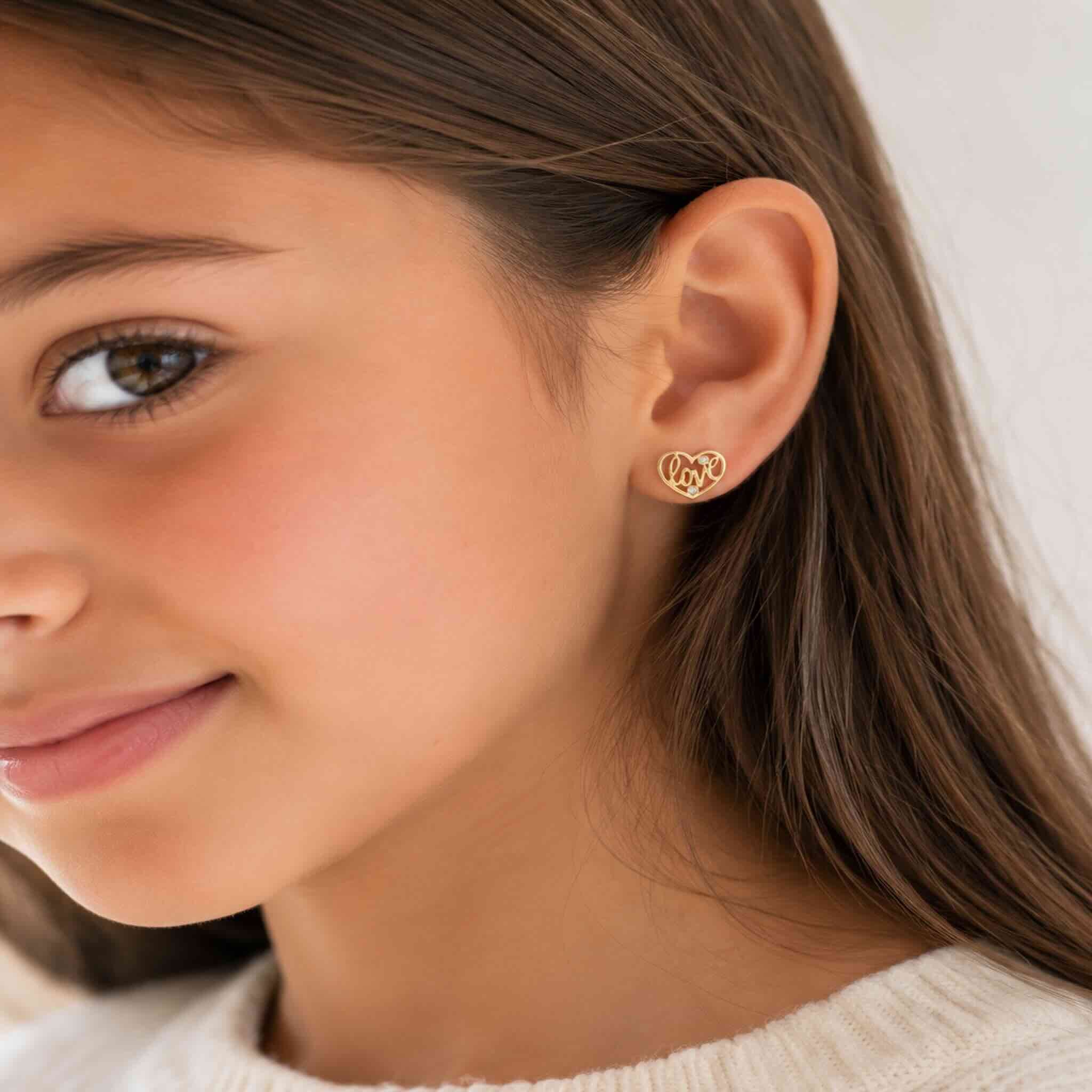 Arete pequeño en Oro 10K con cierre de rosca, diseño corazón Love colocado en la oreja de una niña.