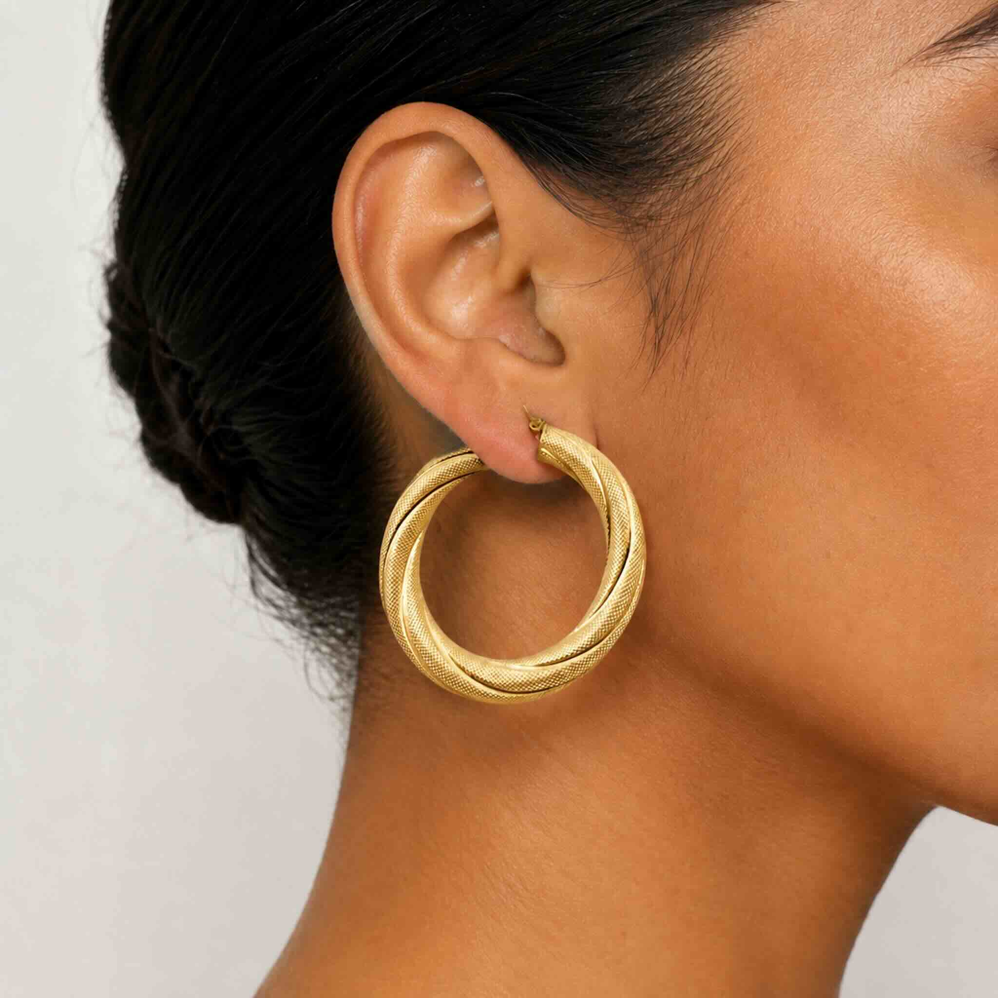 Argollas torcidas satinadas en oro 10K de 6 mm puestas en la oreja de una mujer, estilo grueso y elegante.