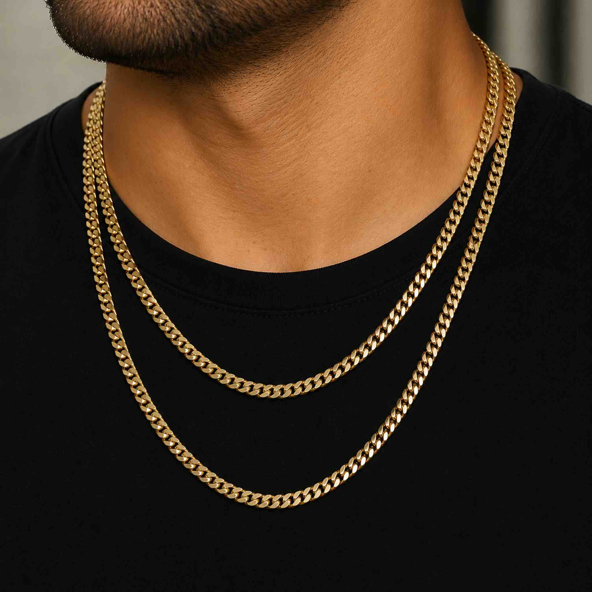 Hombre joven luciendo dos cadenas Cuban Link de oro 10K TuOro en diferentes largos sobre camiseta negra.