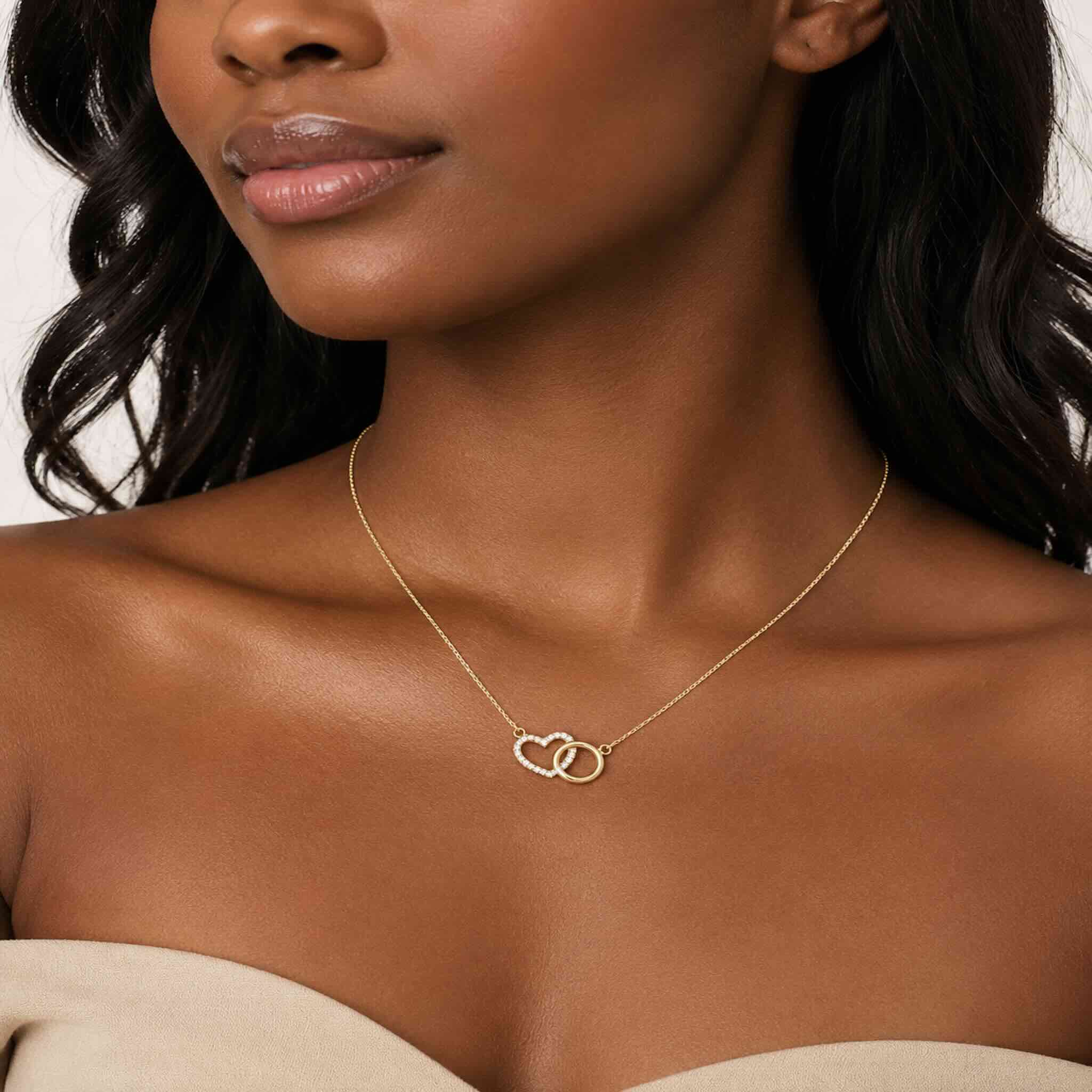 Mujer joven mulata luciendo cadena fina de oro 10K TuOro con dije de corazón con brillo y aro dorado, en foto de cuello y clavícula.