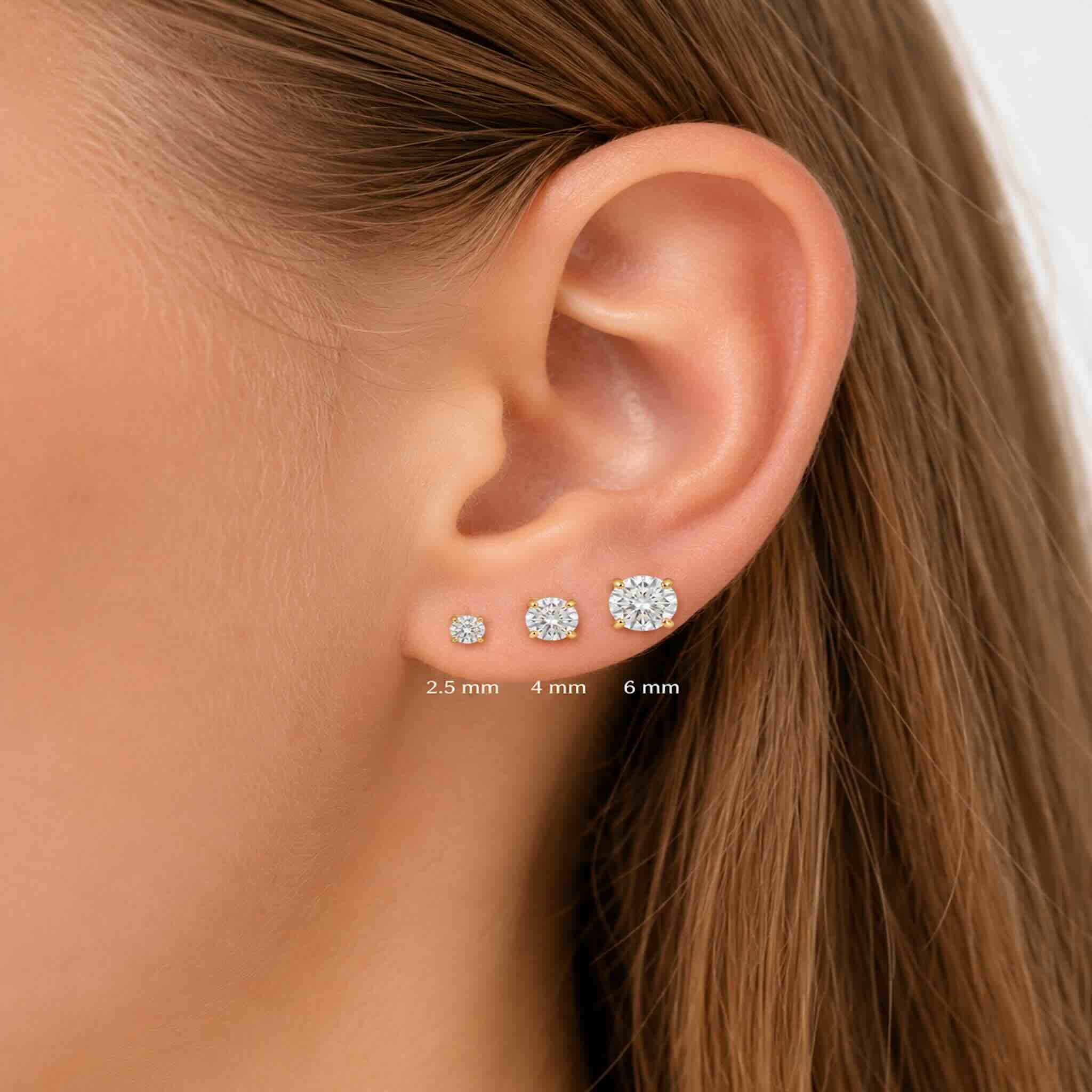Vista de una oreja con tres aretes redondos de circonia transparente en oro 10K, mostrando los tamaños 2.5 mm, 4 mm y 6 mm.