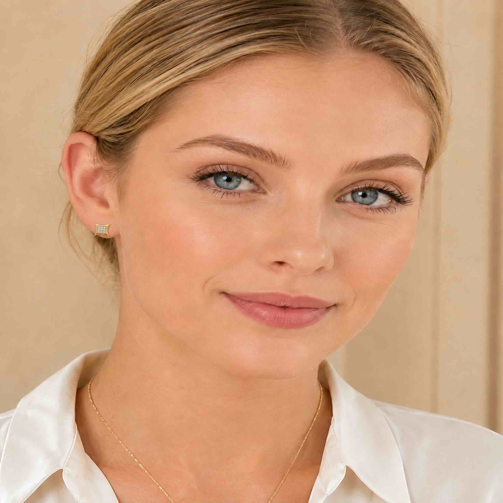 Mujer de ojos claros usando aretes cuadrados pequeños de oro 10K con circonias, tamaño 7 mm.