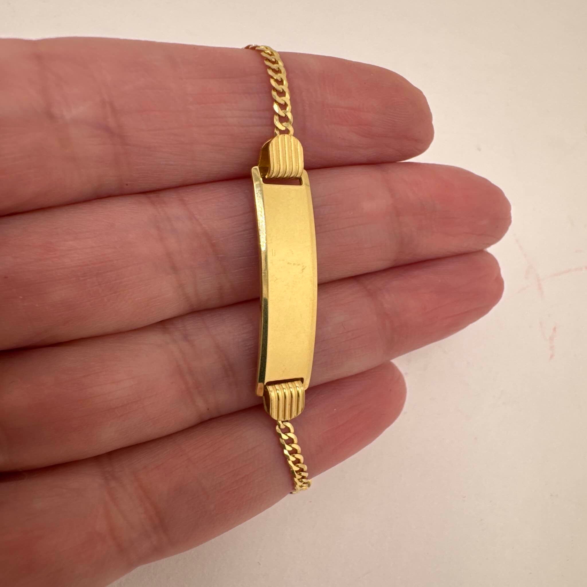 Pulsera Cubana Italiana en Oro 14K 2 mm con placa lisa vista frontal sostenida en la mano de TuOro