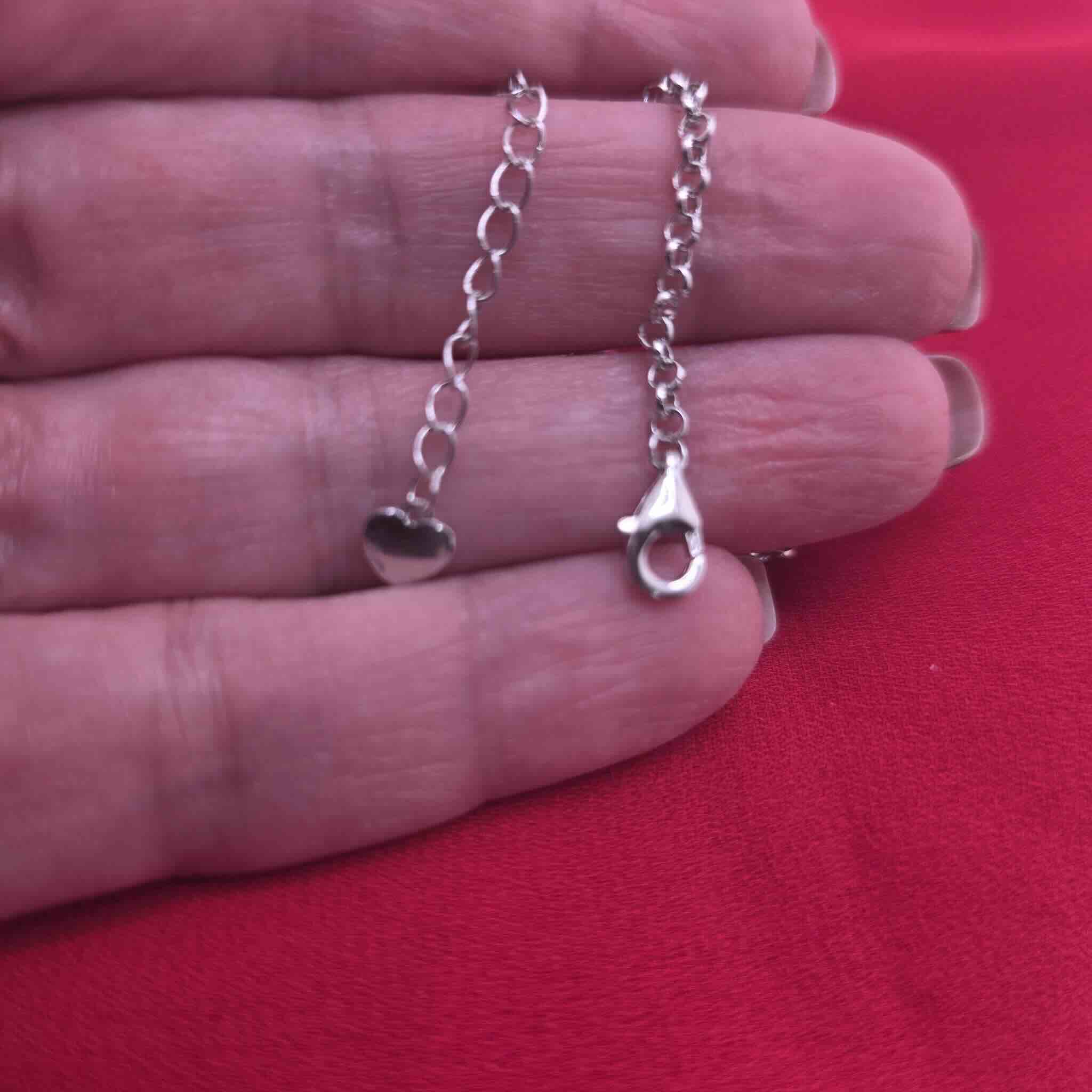 Detalle del cierre y extensión de Pulsera en Plata 925 con dijes esmaltados sobre fondo rojo · TuOro