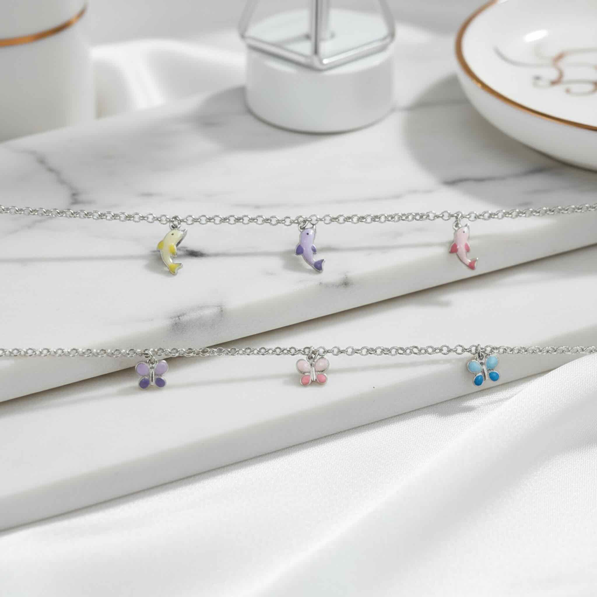 Pulsera en Plata 925 con dijes esmaltados de mariposas y delfines en escena lifestyle elegante sobre superficie de mármol · TuOro