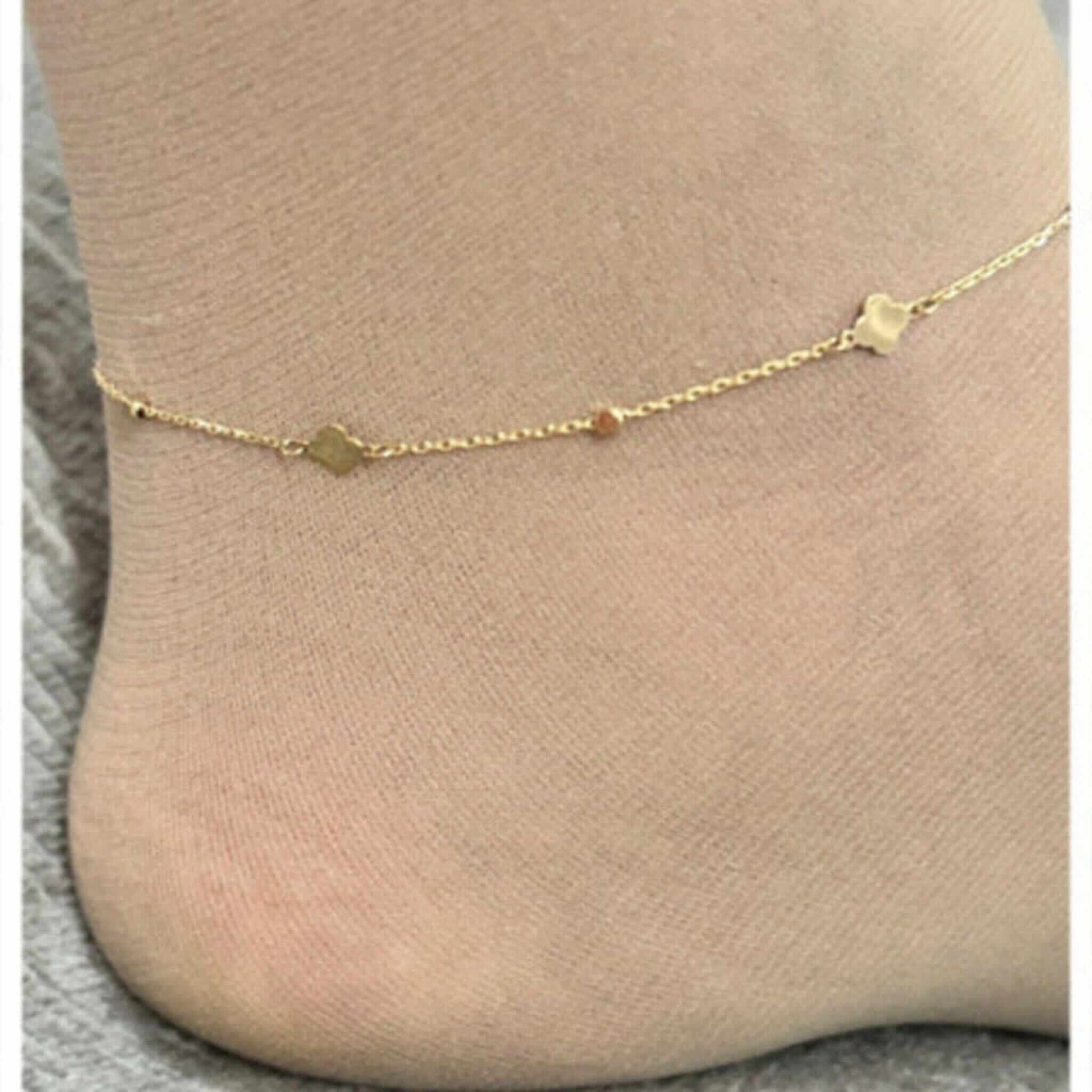 Tobillera fina en Oro 14K con trébol integrado en la cadena, colocada en el tobillo, diseño delicado de Joyería TuOro.